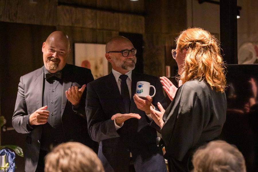 Three people signing and celebrating, one holding a white Dr. Deaf mug